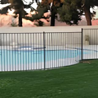 A fenced swimming pool surrounded by grass and trees.