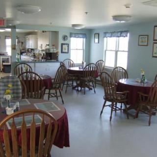 An empty dining area with several tables and chairs, featuring large windows letting in natural light.