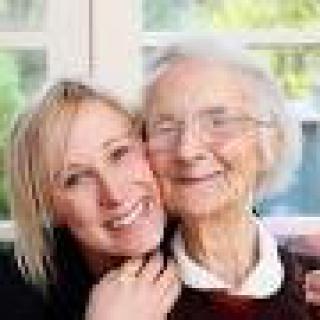 A younger woman and an elderly woman smiling as they pose together indoors.