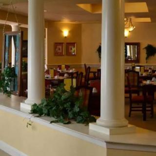 A warmly lit restaurant interior with elegant columns and neatly arranged dining tables.