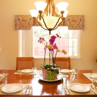 An elegantly set dining table with an orchid centerpiece and chandelier lighting.
