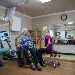 An elderly person sits in a wheelchair while engaging with a therapist in a rehabilitation clinic.