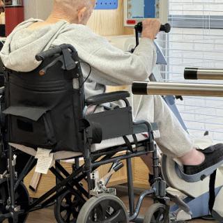 An elderly individual participating in rehabilitation, using a wheelchair during physical therapy.