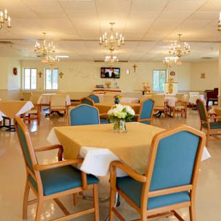 A well-lit dining area with tables and chairs set for guests, featuring elegant chandeliers.