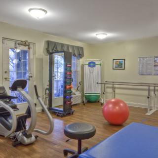 A well-lit gym with various exercise equipment including an elliptical machine, dumbbells, and an exercise ball.