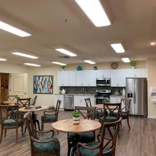 A modern kitchen and dining area with round tables and chairs, featuring stainless steel appliances and bright lighting.
