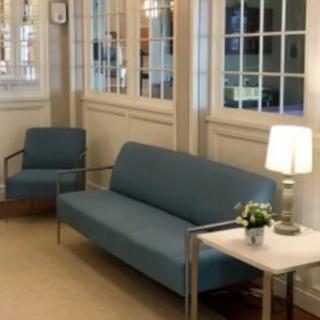 A cozy waiting area with a sofa, armchair, and side table featuring a lamp and decorative plant.
