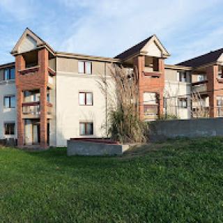 A modern apartment complex featuring multiple balconies and a grassy area in front.