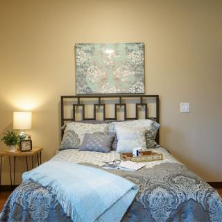 A cozy bedroom with a neatly made bed, decorative pillows, and artwork above the headboard.