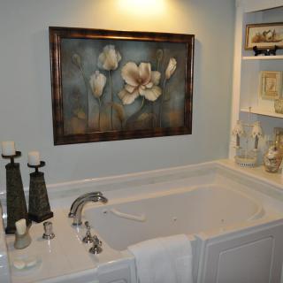 A cozy bathroom with a framed floral artwork above the bathtub and decorative candles on the side.