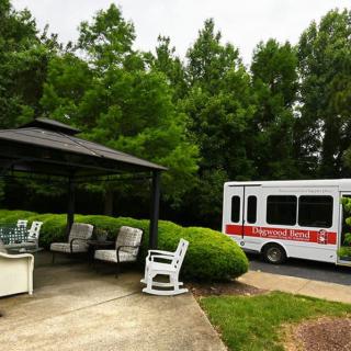 A peaceful outdoor area with a gazebo and seating near a parked bus, surrounded by lush greenery.