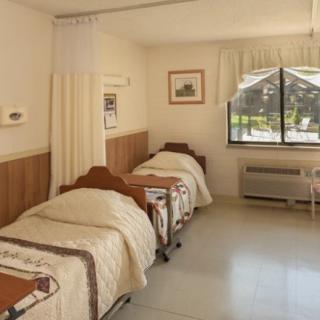 A hospital room with twin beds, separated by a curtain, featuring a large window and air conditioning unit.