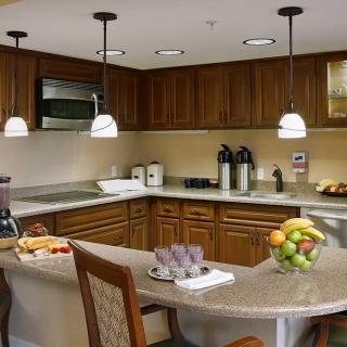 A modern kitchen with wooden cabinets, pendant lighting, and a well-organized countertop featuring appliances and a fruit bowl.