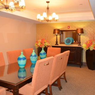 A stylish dining room featuring a glass-topped table with pink upholstered chairs, accentuated by vibrant blue vases and elegant lighting.