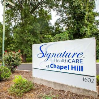 Entrance sign for Signature HealthCARE of Chapel Hill surrounded by greenery.