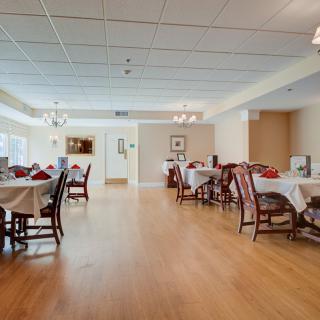 A spacious dining area with neatly arranged tables and chairs, featuring a wooden floor and elegant chandeliers.