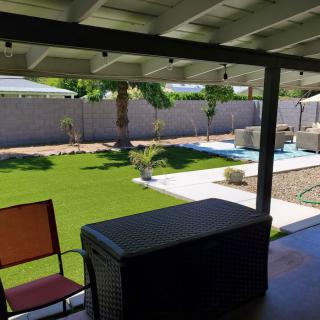 A serene backyard with a patio, lawn, and swimming pool under clear skies.