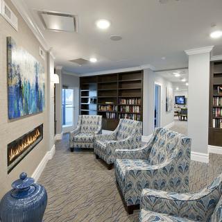 A cozy lobby area featuring a seating arrangement with patterned chairs, a fireplace, artwork on the wall, and bookshelves.