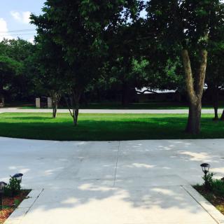 A view of a driveway leading to a grassy area surrounded by trees.