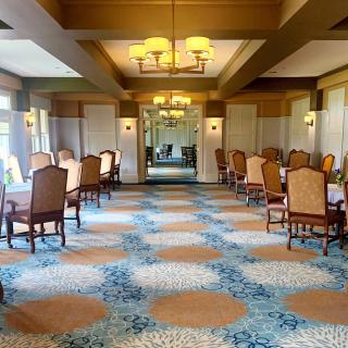 A spacious dining room with elegant chairs and tables, featuring a patterned carpet and ambient lighting.