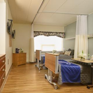 A well-designed hospital patient room featuring two beds, a television, and bright natural light.