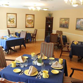 A neatly arranged dining room with blue tablecloths and yellow dishes.