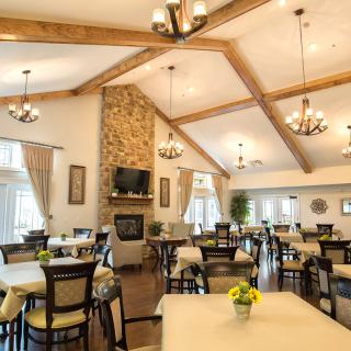 A spacious and well-lit dining area with wooden beams, a stone fireplace, and elegant chandeliers.