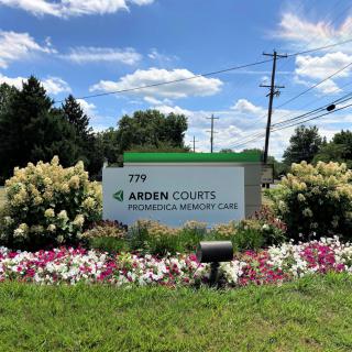 A roadside sign for Arden Courts Promedica Memory Care surrounded by well-maintained landscaping and flowers.