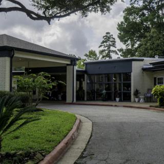 A modern building entrance surrounded by greenery and a curved driveway under a cloudy sky.