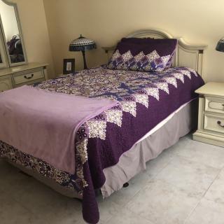A cozy bedroom with a purple quilted bedspread and matching decor.