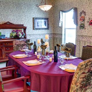 An elegantly decorated dining room with a table set for a formal meal, featuring candles and wine bottles.
