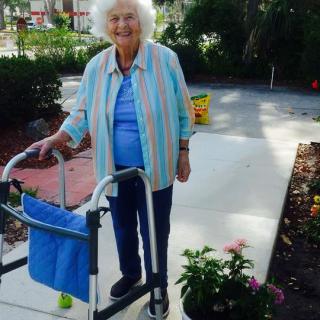 Elderly woman with a walker enjoying gardening outdoors.