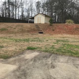 A serene view of a hillside with a small storage building and steps leading up to it, surrounded by grass and trees.