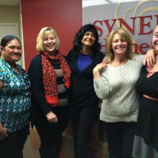 A group of women smiling together in an office setting.