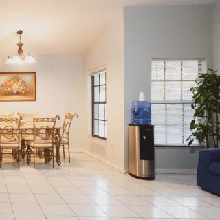 A spacious dining room with a table and chairs, featuring a water cooler and a decorative plant.