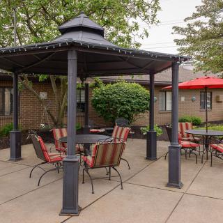 An outdoor patio area featuring a gazebo with chairs and a table, surrounded by trees and additional seating with umbrellas.