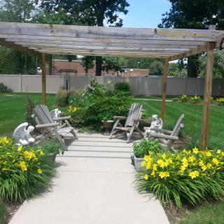 A peaceful garden scene with a pergola, surrounded by flowers and outdoor seating.
