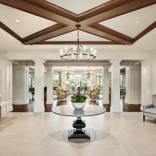 A luxurious foyer featuring a central round table, elegant chandelier, and classical columns.