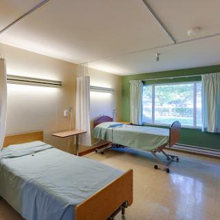 A spacious hospital patient room featuring two beds and natural light from a window.