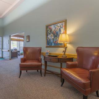 A cozy seating area featuring plush brown chairs, a wooden table with a lamp, and a decorative painting on the wall.