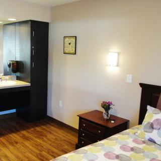 A cozy bedroom with a bed, side table, dresser, and wall-mounted lamp.