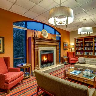 A cozy library with a fireplace, comfortable armchairs, and bookshelves filled with books.