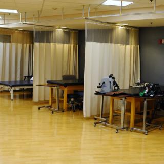 A physical therapy treatment room with multiple tables and equipment, separated by curtains.