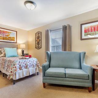 A cozy bedroom with a single bed and a small couch, complemented by wall art and warm lighting.
