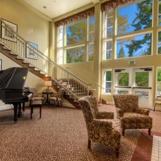 A spacious lobby area featuring a grand piano, a staircase, and large windows with a view of trees.