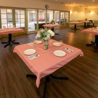 A neatly arranged dining area with tables set for service, featuring pink tablecloths and floral centerpieces.