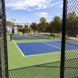 An outdoor pickleball court with a blue and green surface, enclosed by a chain-link fence.