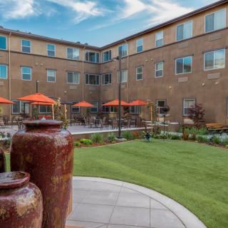 A courtyard with a green lawn and outdoor seating, surrounded by a three-story brick building.