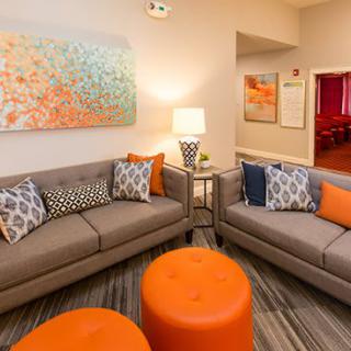 A modern living room with grey sofas and orange accents, featuring contemporary artwork on the wall.
