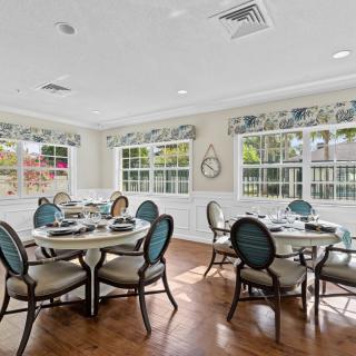 A well-lit dining room with multiple tables and chairs, featuring large windows and elegant decor.
